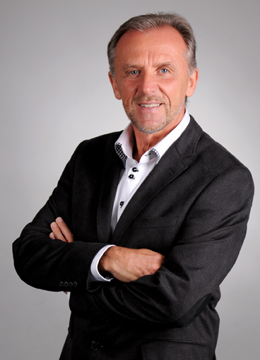 Porträtfoto von Dr. med. Ewald Töth in dunklem Anzug mit gekreuzten Armen vor grauem Hintergrund.