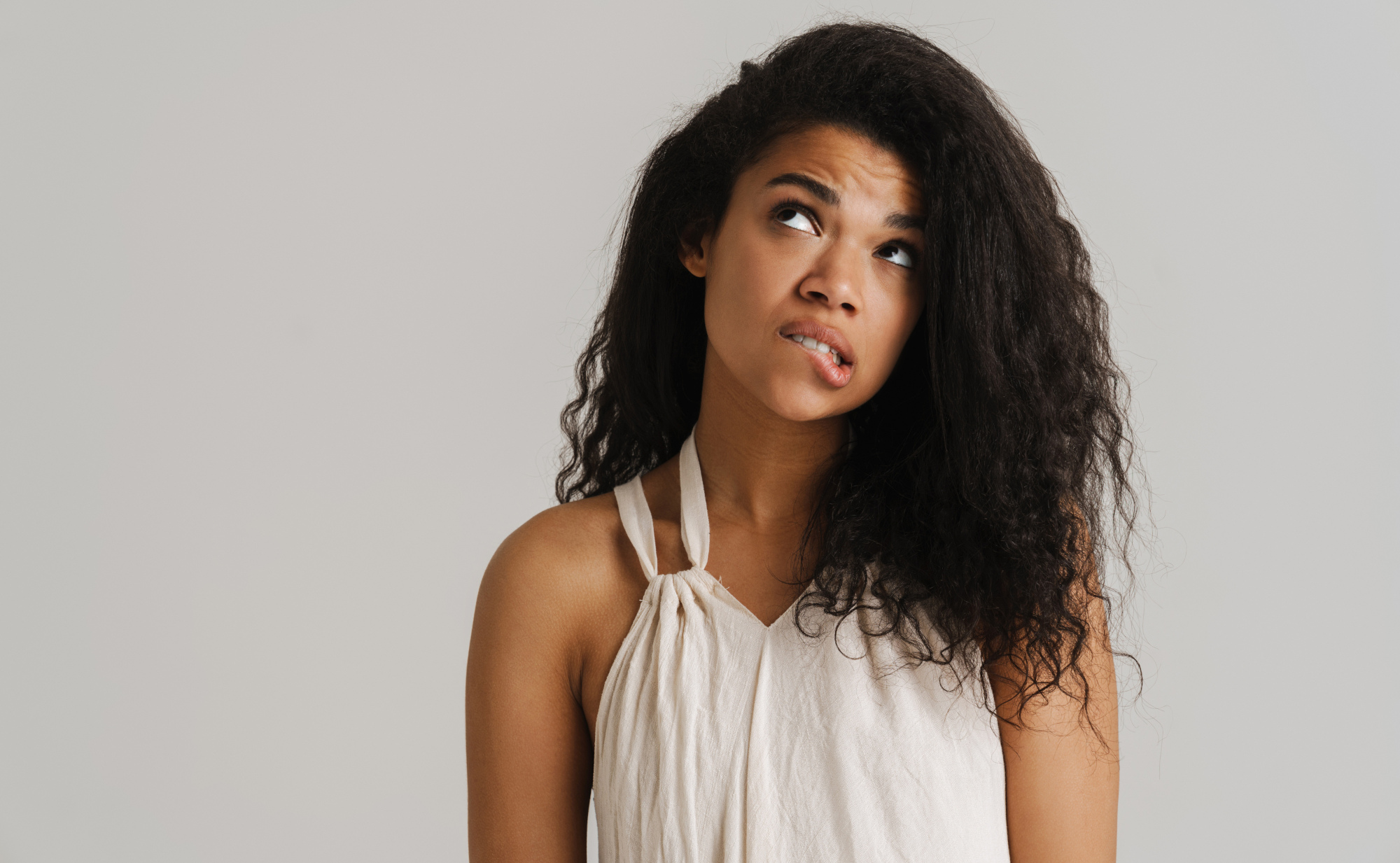 Eine junge Frau mit langen, lockigen Haaren mit zweifelndem Blick nach oben beißt sich leicht auf die Lippe. Symbolfoto für die Rolle des Immunsystems bei Lippenherpes.
