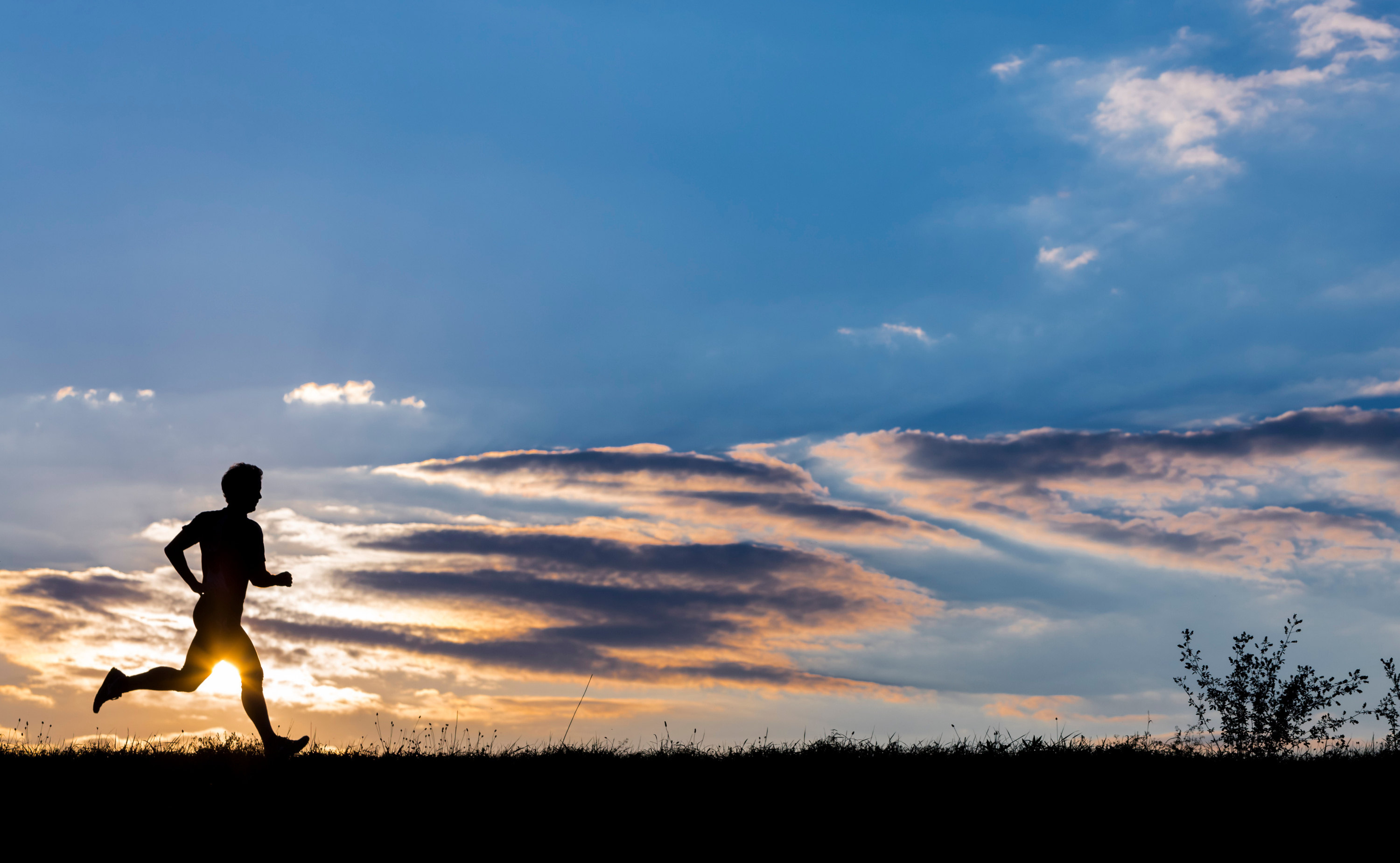 Die Silhouette eines Mannes, der auf einem Hügel im Gegenlicht des Sonnenaufgangs joggt. Ein Symbolfoto für körperliche Energie, die auch durch Magnesium gesteigert wird.