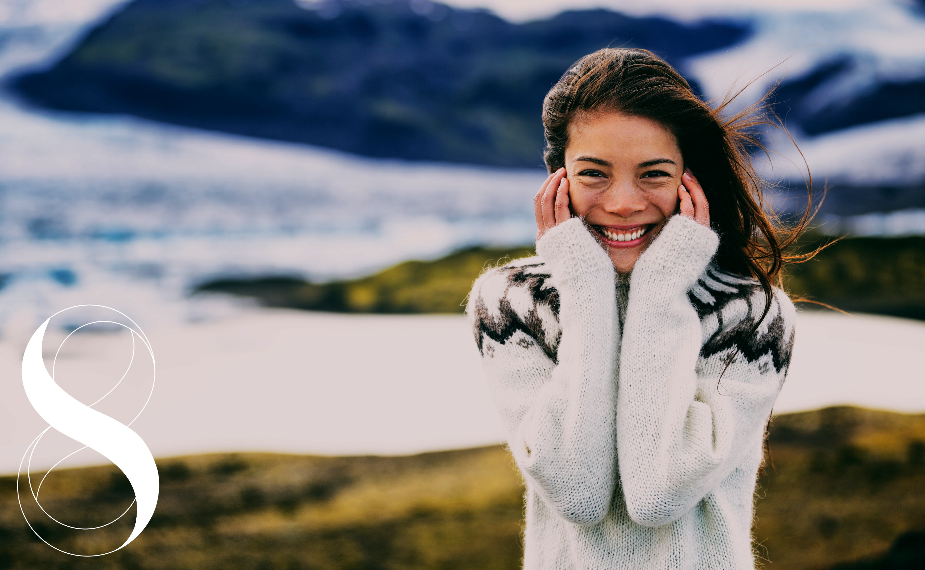 Eine lächelnde Frau in einem hellen Strickpullover hält sich die Hände an die Wangen, im Hintergrund eine nordische Landschaft mit Bergen und Gletschern. Ein Symbolbild von LIFE LIGHT für die lebensnotwendige Wirkung des Spurenelements Zink auf den Körper.